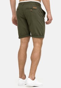 Shorts en coton vert olive avec ourlets retroussés, deux poches latérales et poches arrière décoratives. Dotés d'une étiquette en cuir de marque sur la ceinture.
