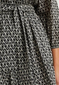Vestido de estampado negro y crema con cintura elástica, detalle de lazo, plisados y mangas cortas con un motivo geométrico.