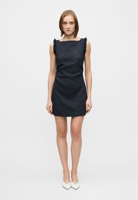 Rochie bleumarin fără mâneci, cu model floral texturat, decolteu pătrat și accente volanate pe umeri, asortată cu pantofi albi cu vârf ascuțit.