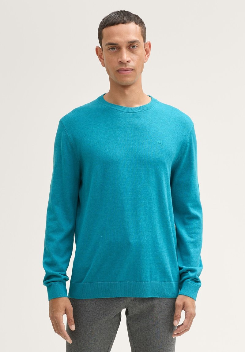 Turquoise gebreide trui, lange mouwen, ronde hals, gemaakt van een zacht materiaal. Bevat een subtiel logo op de borst en geribbelde manchetten.