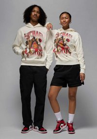 Hupparissa on suuri grafiikkaprintti koripalloilijasta. Miesmallilla on mustat cargo-housut ja naismallilla mustat shortsit. Molemmilla on punavalkoiset lenkkarit.