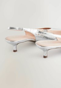 Tacones slingback metálicos plateados con un bajo tacón de kitten, textura suave y plantilla acolchada. El diseño cuenta con sutiles detalles de costura.