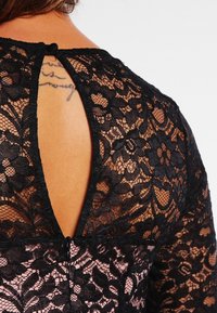 Abito in pizzo nero con un sottofondo colorato, design con cut-out sulla schiena e delicati motivi floreali su tutta la superficie.