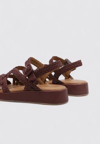 Sandales tressées marron avec une semelle épaisse. Présente des sangles tissées et un détail de boucle. Doublure intérieure lisse, design décontracté.