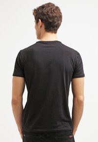Černé tričko s krátkým rukávem vyrobené z měkké tkaniny, s klasickým kulatým výstřihem a přiléhavým střihem, zobrazené zezadu.