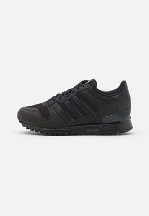 Baskets Adidas noires avec mesh, accents en cuir, design à lacets et semelle texturée pour l'adhérence, montrées en profil sur fond blanc.