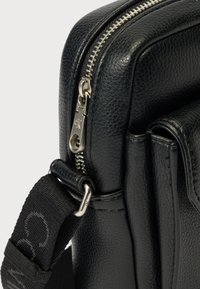 Must nahast kott, millel on tekstuuriga viimistlus, hõbedane tõmblukk ja eemaldatav rihm koos logoga. Kompaktne disain mitme taskuga.