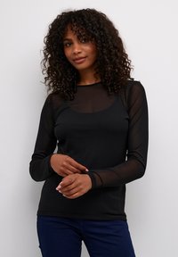 Haut noir à manches longues en matière transparente, pr�ésentant un col rond et une silhouette ajustée. Le modèle le porte avec un jeans bleu foncé.