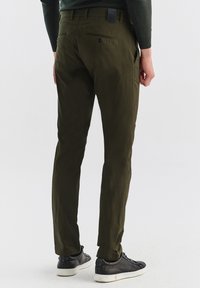 Ciemnozielone spodnie o slim fit, z tylną kieszenią i szlufkami na pasek, noszone z czarnymi sneakersami. Gładka tekstura, casualowy design.