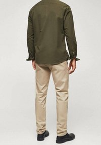 Camisa de manga larga color verde oliva, pantalones ajustados beige, zapatos negros, tela texturizada, diseño entallado y detalles de costuras visibles.