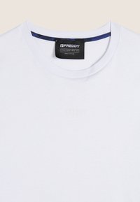 T-shirt bianco in cotone con scollo rotondo, dotato di un'etichetta blu scuro. Logo goffrato discreto sul davanti, texture liscia.