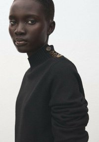 Schwarzer Strick-Turtleneck-Pullover mit strukturiertem Ripp-Design und Knopfakzenten auf der Schulter, mit einer figurbetonten Passform und langen Ärmeln.