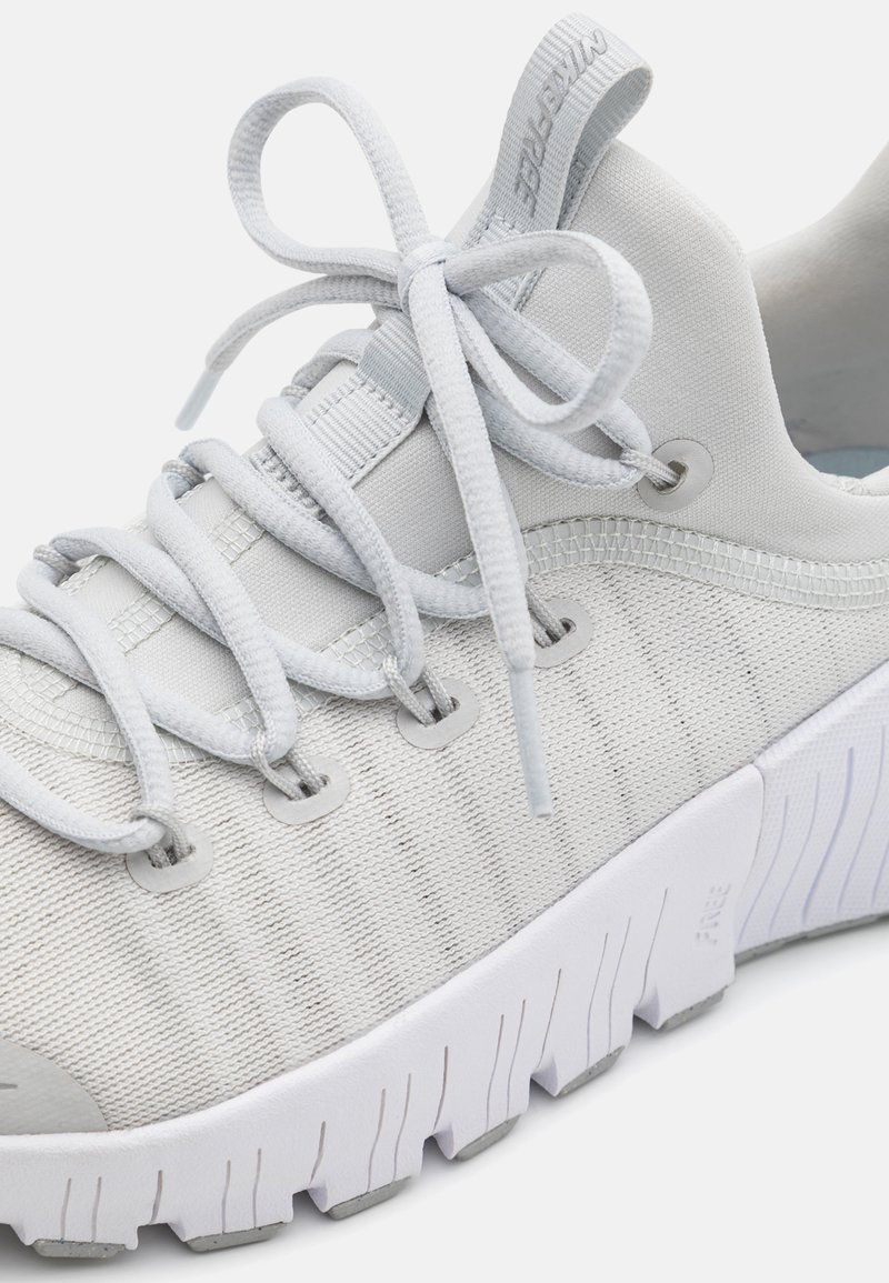 Scarpa sportiva grigia chiara con tomaia in rete testurizzata, suola bianca a contrasto, lacci piatti e asole rinforzate per una maggiore durata.