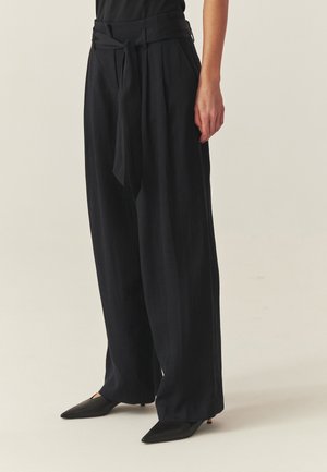 Black high-waist wide-leg pants with tied belt and pleats, worn with black pointy-toe heels, shown from waist to feet.