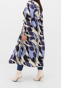 Pitkä, kuvioitu mekko sinisessä, mustassa ja kremessä, jossa on kerrattu vyötärö, yhdistettynä tiukkoihin farkkuihin ja vaaleanbeigeihin korkokenkiin, joissa on nilkkaremmitys.