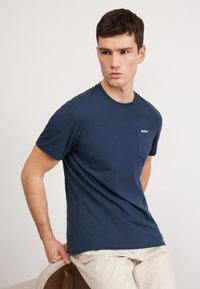 Navy blue cotton t-shirt with short sleeves, crew neck, and a small chest pocket featuring white logo detail. Smooth texture, casual fit.