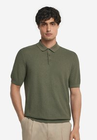 Piké i strukturerad mörkgrön tyg med korta ärmar och krage med knappar, som har ribbade kantar och muddar.