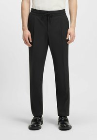 Black tailored pants with an elastic waistband and drawstring. Features two side pockets and a smooth, sleek fabric finish.