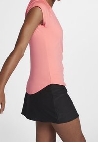 Top atlético de mangas cortas en un vibrante color rosa, combinado con una falda negra acampanada. Tejido suave con una silueta ajustada y dobladillo redondeado.