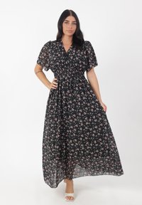 Maxi-jurk van doorschijnende zwarte stof met een bloemenpatroon in roze en groen. Heeft pofmouwen, een getailleerde taille en een vloeiende rok.