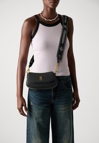 Sac en cuir noir à bandoulière avec un design structuré, accent en logo doré, et une sangle ajustable à motif arborant le texte "Stella McCartney".