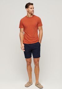 Roestoranje T-shirt met ronde hals, marineblauwe gestreepte shorts en beige instappers. Katoenen stof met een casual pasvorm, geen zichtbare logo's.