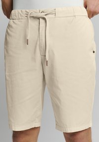 Beige zwembroek van lichtgewicht stof, met een elastische tailleband met trekkoord, zijzakken en een relaxte pasvorm.