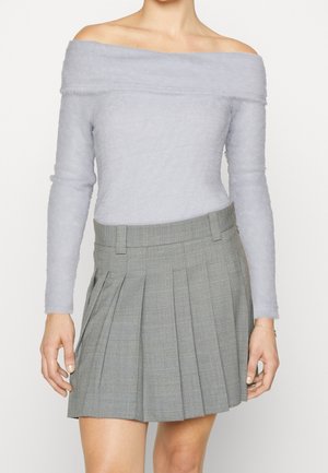 Femme portant un haut gris clair à manches longues duveteux et à épaules dénudées, ainsi qu'une mini-jupe plissée à carreaux grise taille haute.