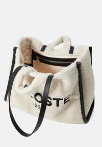 Borsa in pile crema con accenti e cinturini in pelle nera. Presenta una tasca interna con cerniera e un logo ricamato sul lato.
