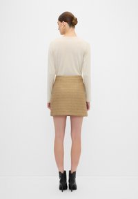 Ljusbeige långärmad skjorta i kombination med en strukturerad tan minikjol. Svarta ankelstövlar fulländar outfiten. Enkelt, minimalistiskt design.