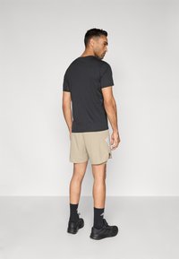 Zwart kort shirt met korte mouwen, beige sportshorts met zijaccenten, zwarte sokken en zwarte sneakers, gezien van achteren. Strak, minimalistisch ontwerp.