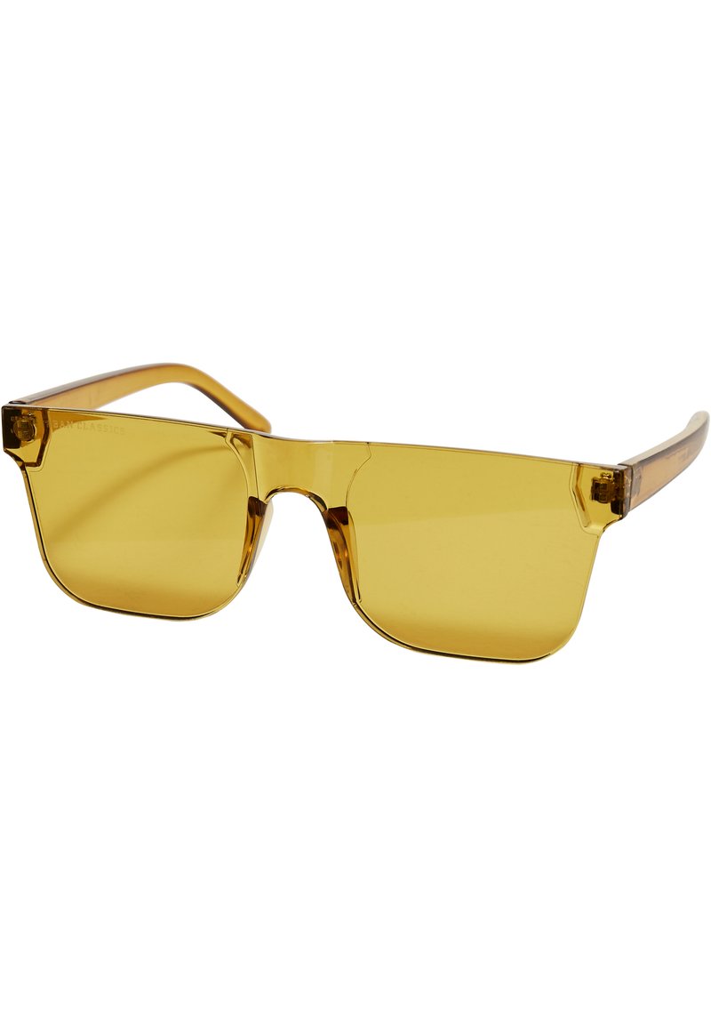Ochelari de soare galbeni cu un cadru geometric, brațe transparente și lentile plate. Materialul pare a fi plastic cu o textură netedă.