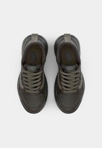 Dark brown Vans sneakers featuring a textured upper, rounded toe, and grey laces. Includes a pull tab on the heel and logo detail.