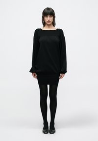 Čierne šaty s dlhým rukávom, voľného strihu so zaviazaním v páse. Majú štvorcový výstrih a rebrovanú textúru. Kombinované s čiernymi pančuchami a topánkami.