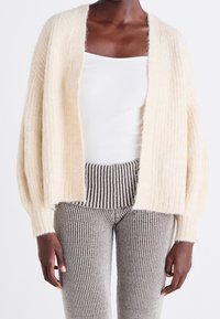 Beige fluffy cardigan with open front and textured ribbing, paired with fitted gray and white striped ribbed pants.
