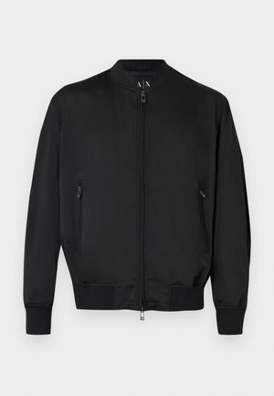 Μαύρο bomber τζάκετ με φερμουάρ μπροστά, τσεπάκια με φερμουάρ στο πλάι, ριμπ μανσέτες και τελείωμα, και ένα μικρό ανάγλυφο λογότυπο στο στήθος.