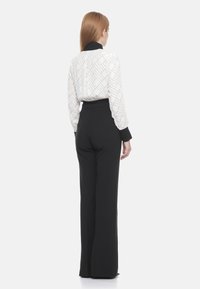 Camicia bianca a maniche lunghe con colletto nero e motivo geometrico, abbinata a pantaloni neri a vita alta, con gambe ampie e texture liscia.