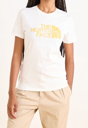 Vitt bomullströja med korta ärmar med en gul grafisk logotyp "THE NORTH FACE" på framsidan. Avslappnad passform och mjuk textur.