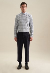 Camicia a quadri bianca e blu navy, abbinata a pantaloni scuri e scarpe nere. Vestibilità strutturata, infilata dentro con un colletto ordinato.