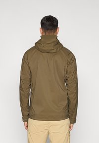 Πράσινο μπουφάν ελιάς με ψηλό γιακά και κουκούλα. Λείο ύφασμα ανθεκτικό στο νερό. Μακριά μανίκια με ρυθμιζόμενες μανσέτες. Πλάγια όψη από πίσω.