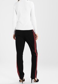 Bílý top s dlouhým rukávem v kombinaci s černými kalhotami s červenými a bílými pruhy po bocích. Oblečení má úzký a přiléhavý střih.