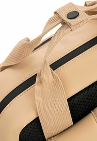Borsa impermeabile beige con tracolle nere, caratterizzata da una rete nera testurizzata e cuciture a macchina. Include una chiusura a scatto per un fissaggio sicuro.