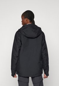 Sort vandtæt jakke med en tætsiddende hætte, glat tekstur og justerbare manchetter, vist fra ryggen. Minimalistisk design uden synlige logoer.