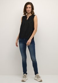 Blusa nera senza maniche con scollatura a V e una sottile trama a righe, abbinata a jeans blu aderenti e sneakers di colore chiaro.