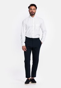 Wit lange mouw knoopshirt met een borstzak, gecombineerd met donkerblauwe slim-fit broek en zwarte instap schoenen.