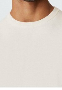Camiseta de cuello redondo de color beige claro, hecha de algodón suave, con una textura lisa y un diseño sencillo sin patrones ni acentos.