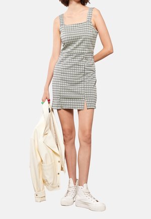 Vestido mini de cuadros con escote cuadrado, fruncido en la cintura, abertura lateral; combinado con una chaqueta crema y zapatillas blancas de caña alta.