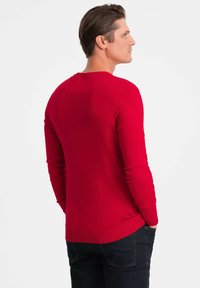 Pullover en coton rouge à manches longues avec un col rond, des poignets et un ourlet côtelés, texture lisse et silhouette ajustée. Présenté de dos.