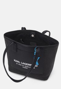 Sac fourre-tout tissé noir avec des accents en cuir lisse, doté d'une étiquette logo bleue et de poignées tressées. Poche intérieure pour un rangement sécurisé.
