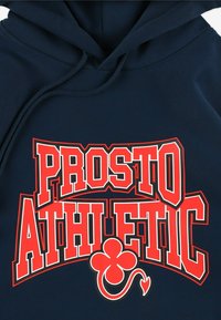 Granatowa bluza z kapturem z napisem "PROSTO ATHLETIC" w wyraźnej czerwonej i białej czcionce; posiada grafikę zielonego koniczyna z krętym ogonkiem.